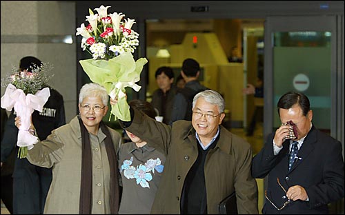 6일 오후 인천공항을 통해 입국한 로버트 김(64ㆍ김채곤)과 부인 장명희씨가 취재진을 향해 꽃다발을 들고 있는 가운데 백동일 예비역 대령이 눈물을 닦고 있다. 